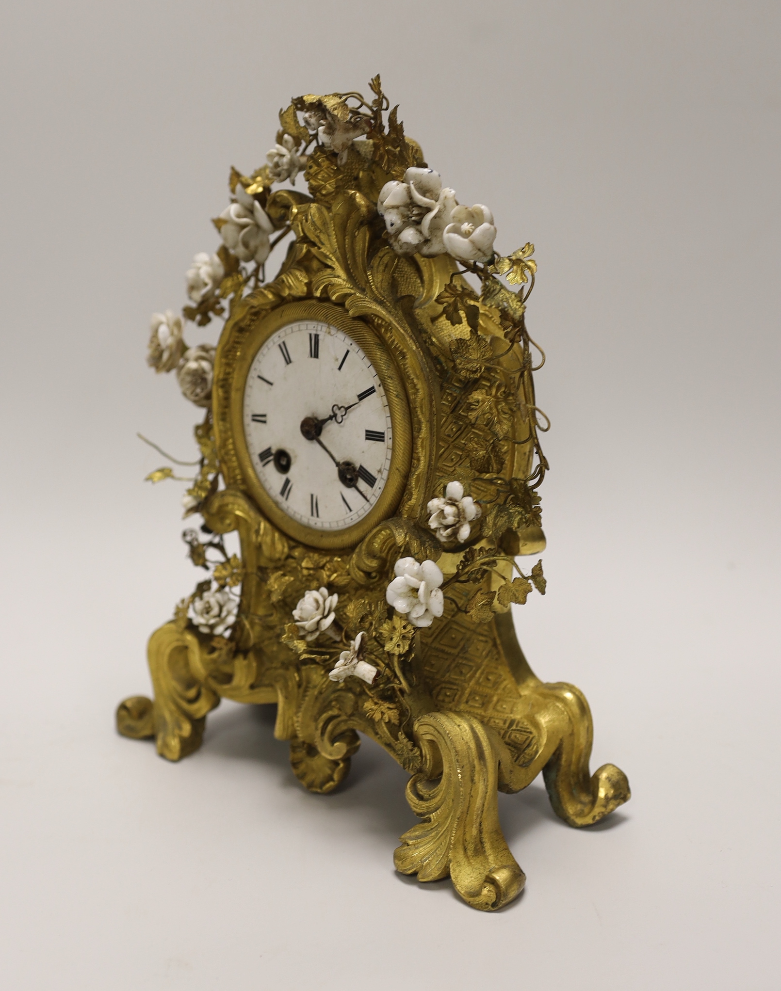 A 19th century gilt bronze and porcelain mounted mantel clock, the waisted case cast with rocaille, embellished with porcelain flower heads, with circular white enamel Roman dial, the associated twin train movement with